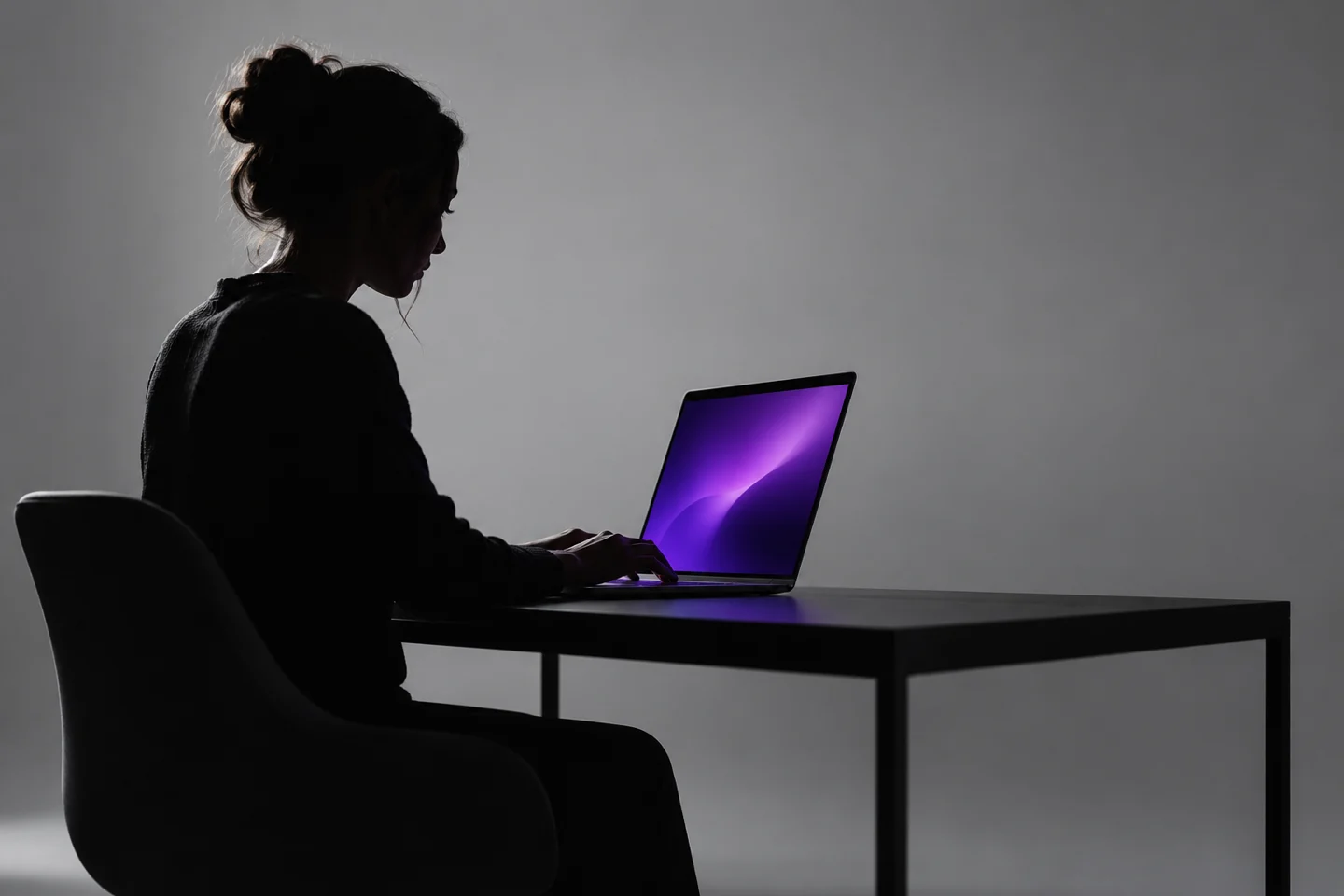 Concept image of a person in shadow working on a purple-lit laptop