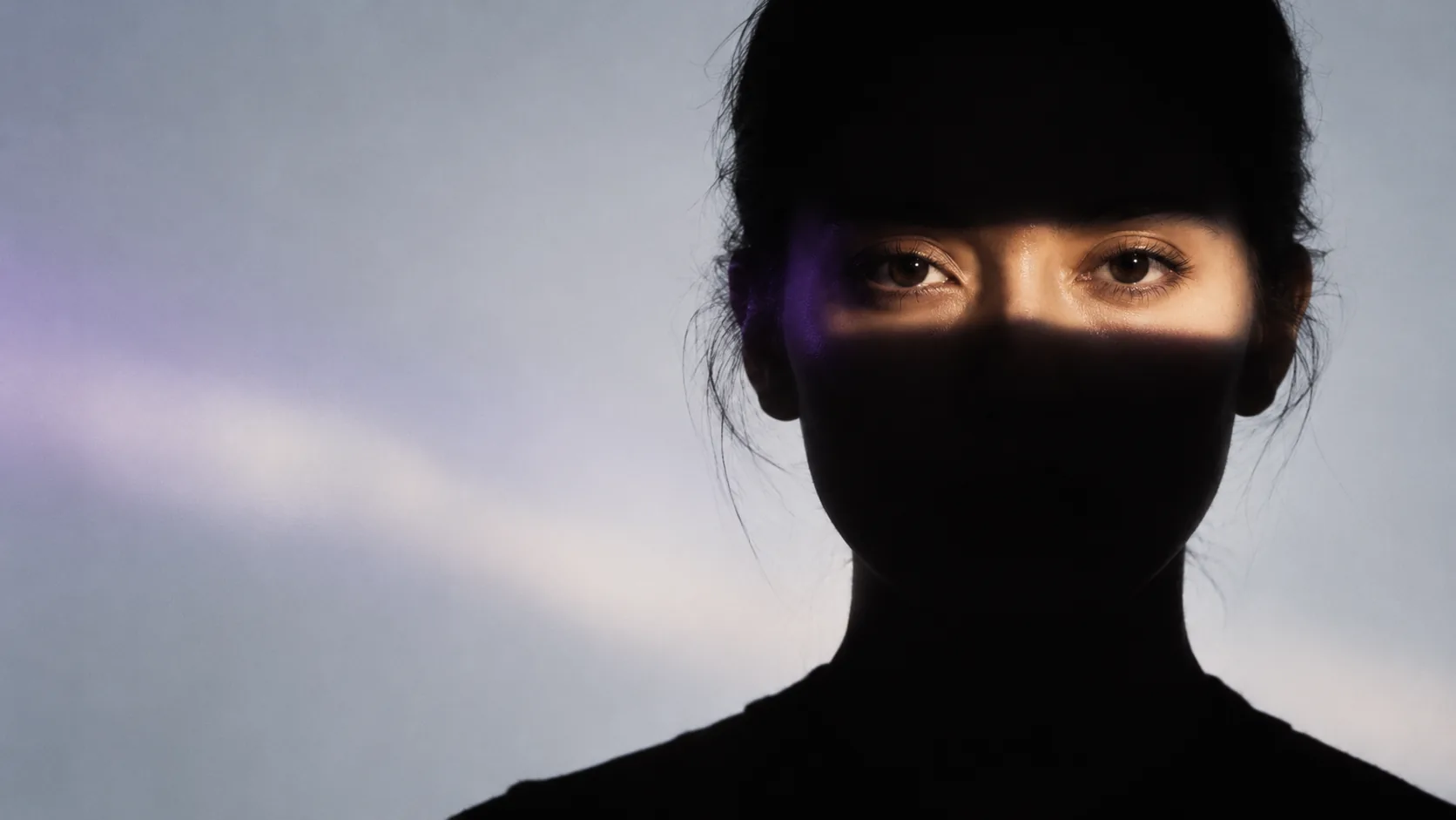 Conceptual image of a woman in silhouette with one eye revealed by controlled light