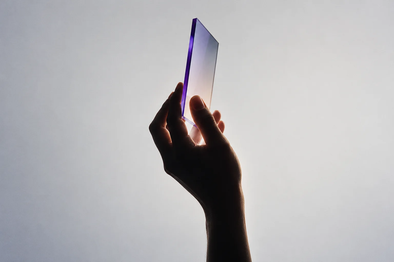 A silhouetted hand holding an optical glass plane in controlled light, representing focused automation