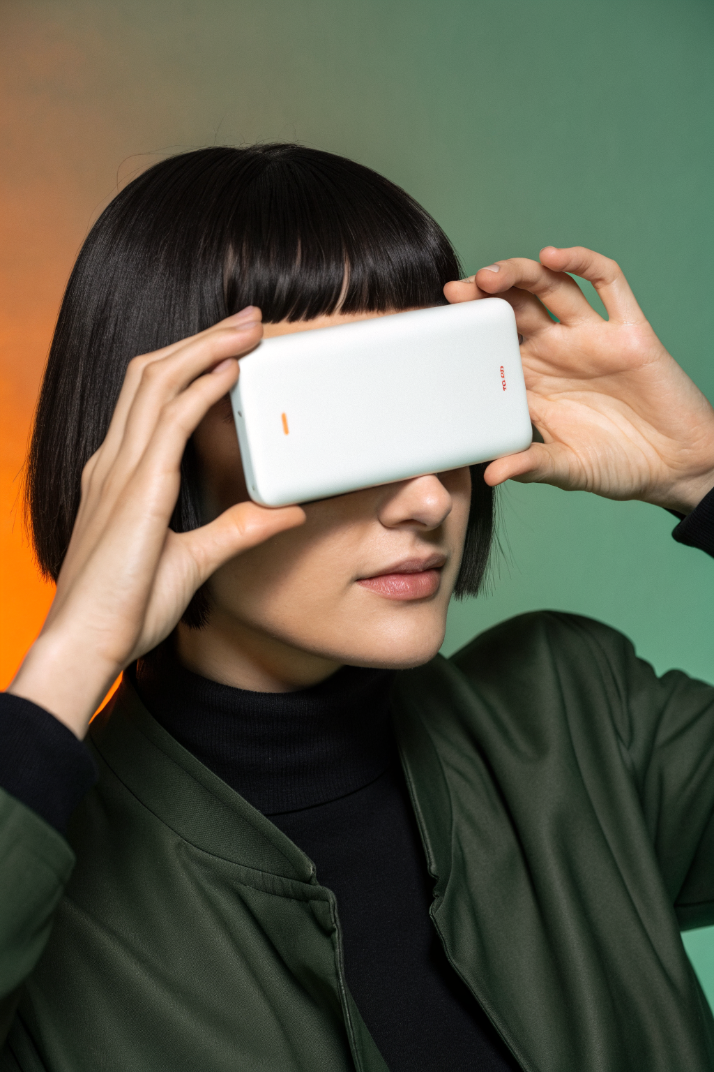 Close-up of a person holding a sleek white device over one eye against a muted green background, with warm orange glow