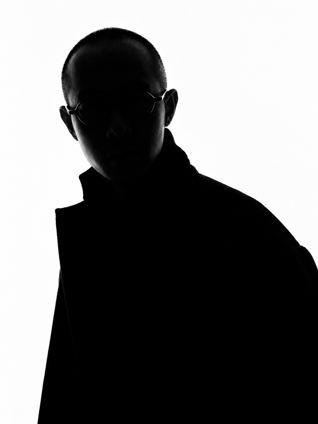 Backlit silhouette with round glasses against a white studio backdrop