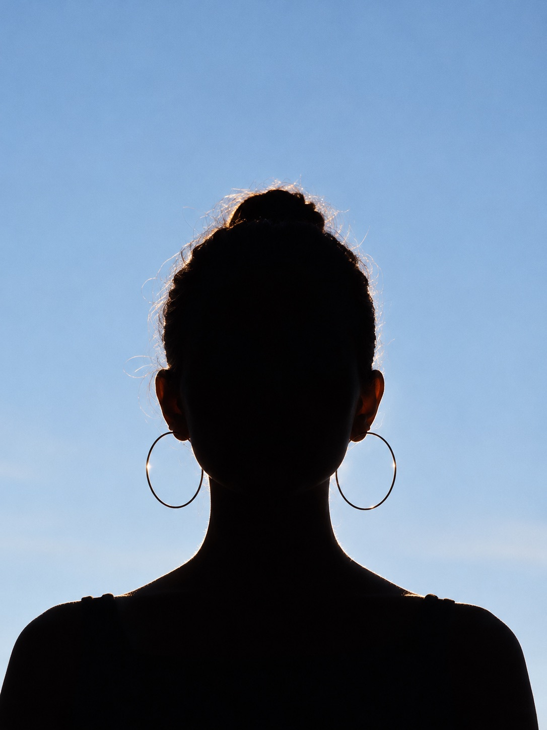 Silhouette with hoop earrings rim lit against a clear blue sky