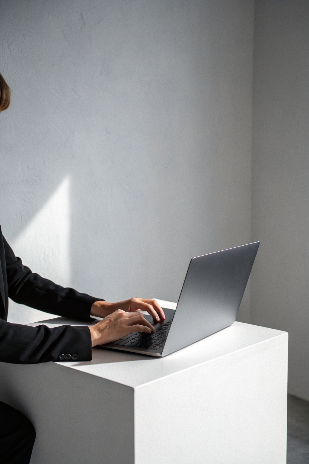 Minimalist editorial photo of hands typing on a laptop on a white table, with empty grey wall above